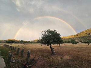 Full Rainbow over Large Ranch Property with Shrubs and Rocky Hills